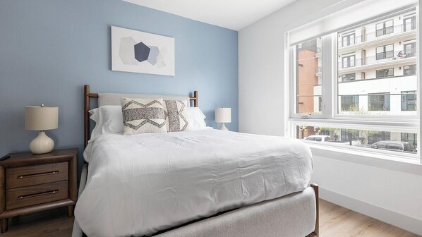 A bedroom with a bed, two bedside tables, a window, and a city view. - Landing | Chic Studio, Rooftop Lounge, Game Room (Austin)