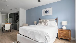A bedroom with a bed, bedside tables, a desk, and a kitchenette. - Landing | Chic Studio, Rooftop Lounge, Game Room (Austin)