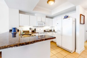 A kitchen with white cabinets, a white refrigerator, a microwave, and a granite countertop. - Bright & breezy condo with Gulf view, pools & beach access (Gulf Shores)
