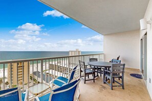 A balcony with a view of the beach and ocean, a table with chairs, and a small table with a chair. - Bright & breezy condo with Gulf view, pools & beach access (Gulf Shores)