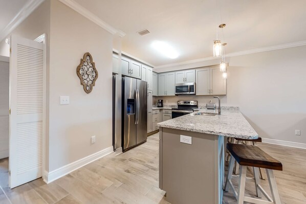 A modern kitchen with a stainless steel refrigerator, a microwave, and a granite countertop. - Dog-Friendly Condo with Shared Pool, Central AC, & Free High-Speed WiFi (Gulf Shores)