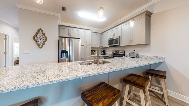 A modern kitchen with granite countertops, stainless steel appliances, and wooden bar stools. - Dog-Friendly Condo with Shared Pool, Central AC, & Free High-Speed WiFi (Gulf Shores)