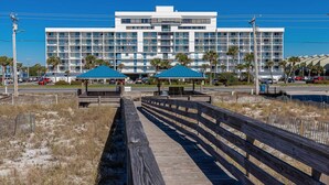 A modern hotel with a long wooden boardwalk leading to a covered area with two blue umbrellas. - Inviting Condo w/ Shared Pools, Hot Tub, Tennis, & Beach Access (Gulf Shores)