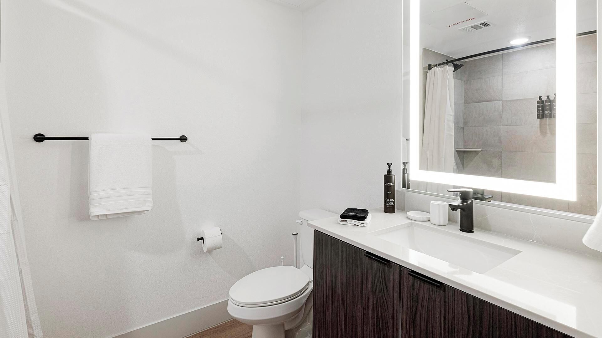 Une salle de bain moderne avec des toilettes blanches, un lavabo avec un miroir et un espace douche.