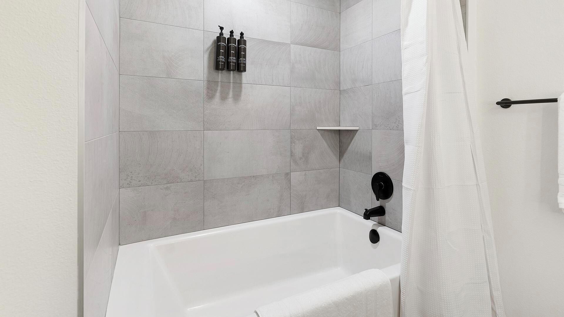Un bagno con una vasca da bagno bianca, piastrelle grigie e una tenda da doccia.