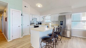 A modern kitchen with a central island, stainless steel appliances, and a dining area with four chairs. - Spacious, Gulf-front vacation home with covered deck & beach access (Gulf Shores)