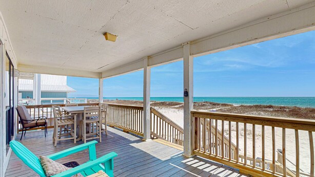 A wooden deck with a table and chairs, a bench, and a view of the beach. - Spacious, Gulf-front vacation home with covered deck & beach access (Gulf Shores)