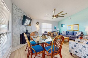 Un salon avec un mur en pierre, un téléviseur à écran plat, un ventilateur de plafond, une table à manger avec des chaises, un canapé et une table basse.