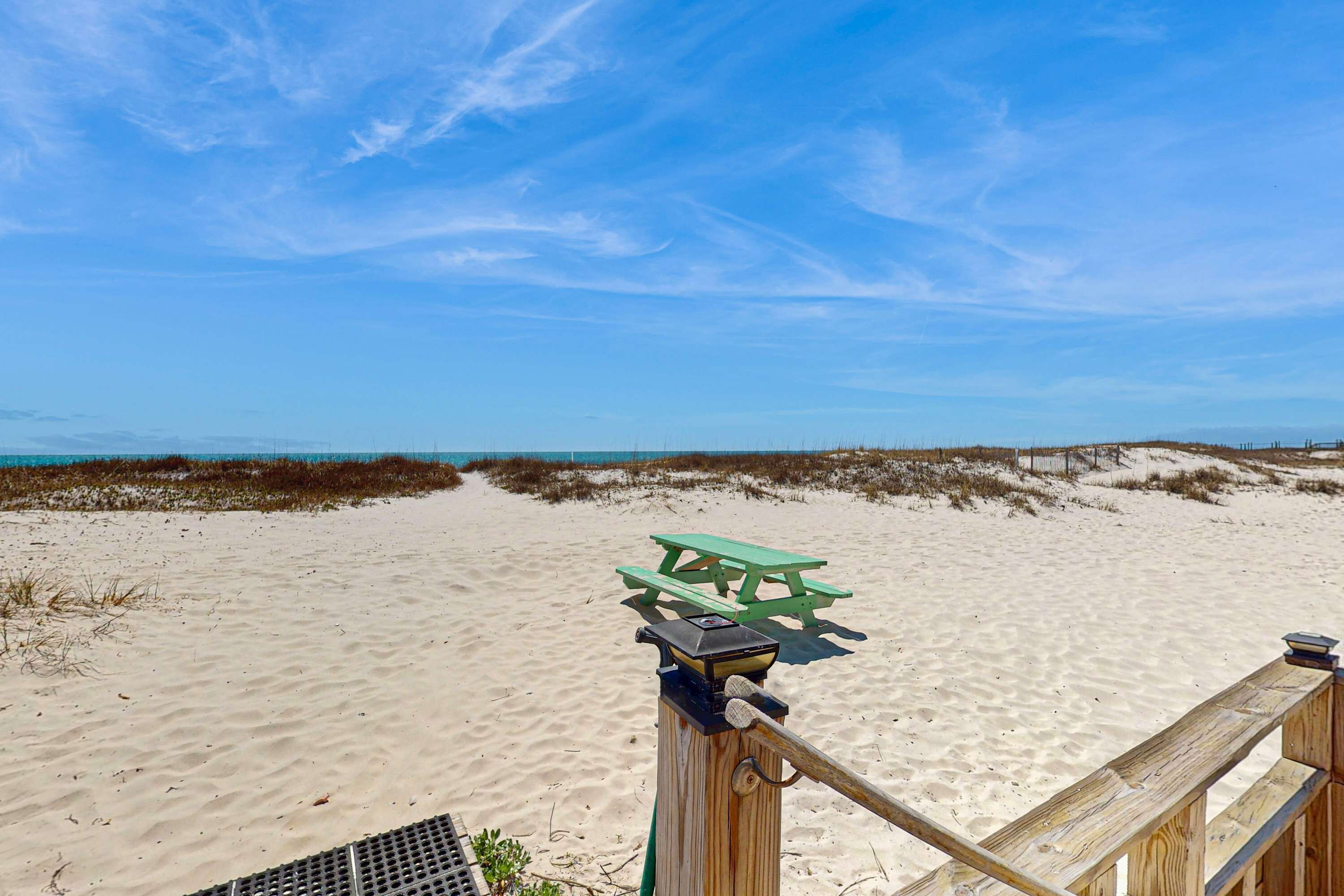Una spiaggia sabbiosa con un pontile di legno e un tavolo da picnic verde.