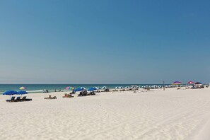 A beach with rows of sun loungers and umbrellas, a clear sky, and the ocean in the background. - Spacious, Gulf-front vacation home with covered deck & beach access (Gulf Shores)