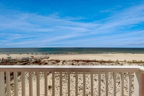 A beach view from a balcony with a wooden railing, sandy beach, and a clear sky. - Memorable & group-friendly house w/Gulf views and private sun deck (Gulf Shores)