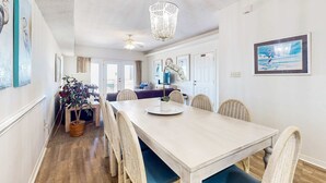 A dining area with a long table, wicker chairs, a chandelier, and artwork on the walls. - Two homes in one - beachfront, Gulf-view decks, central AC & washer dryers (Gulf Shores)