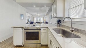A modern kitchen with built-in appliances, a marble countertop, and a large window with blinds. - Two homes in one - beachfront, Gulf-view decks, central AC & washer dryers (Gulf Shores)