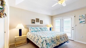 A bedroom with a bed, two bedside lamps, a ceiling fan, a door with a view, and three framed pictures on the wall. - Two homes in one - beachfront, Gulf-view decks, central AC & washer dryers (Gulf Shores)