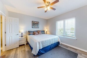 Ein Schlafzimmer mit einem Bett, Nachttischen, einem Deckenventilator, einem Fenster mit Jalousien und einer Tür.