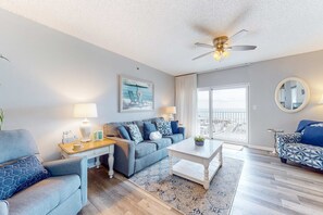 A modern living room with a sofa, coffee table, and a ceiling fan. - Gulf front, corner condo w a private balcony plus a shared beachside pool (Gulf Shores)