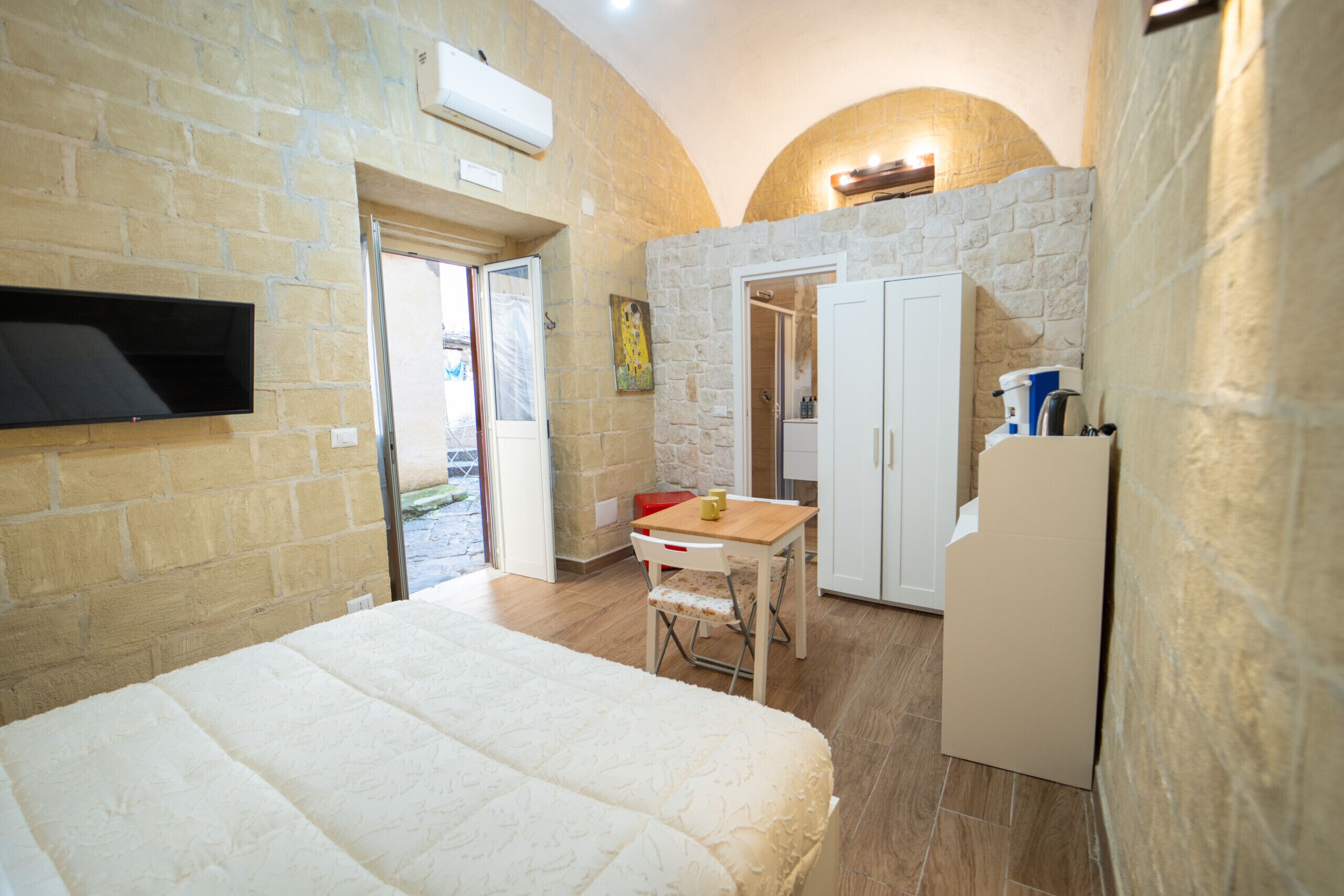 Een slaapkamer met een bed, een bureau, een stoel, een kledingkast en een kleine kitchenette.