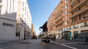 Une place publique avec une statue de cheval, des bâtiments dotés de balcons et un ciel dégagé.