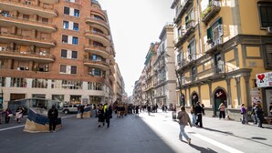 Une rue animée en milieu urbain, bordée d’immeubles à plusieurs étages, avec des piétons et un ciel dégagé.