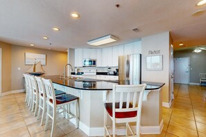 A modern kitchen with white cabinetry, a central island, and a seating area with white chairs. - Beachfront corner penthouse w/ amazing view, balcony & shared pools/hot tubs (Gulf Shores)
