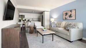 A modern living room with a sofa, coffee table, TV, and kitchen in the background.