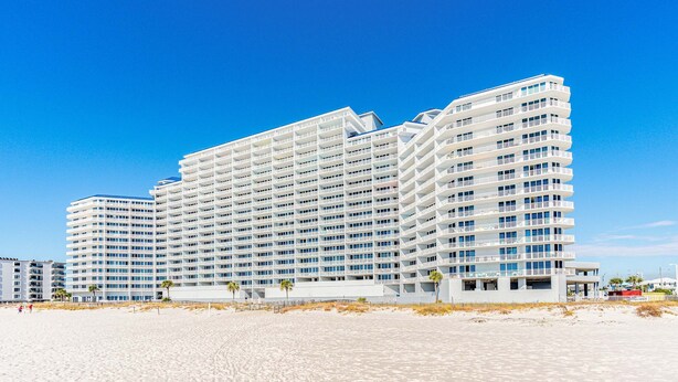 Un hotel moderno de varios pisos, situado en una playa bajo un cielo azul cristalino.