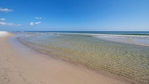 Ein Strand mit klarem Wasser, sandigem Ufer und blauem Himmel.
