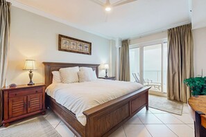 A bedroom with a large bed, wooden nightstands, a ceiling fan, a balcony with curtains, and a framed picture on the wall. - Condo with great views, two pools, & private balcony - near attractions (Gulf Shores)
