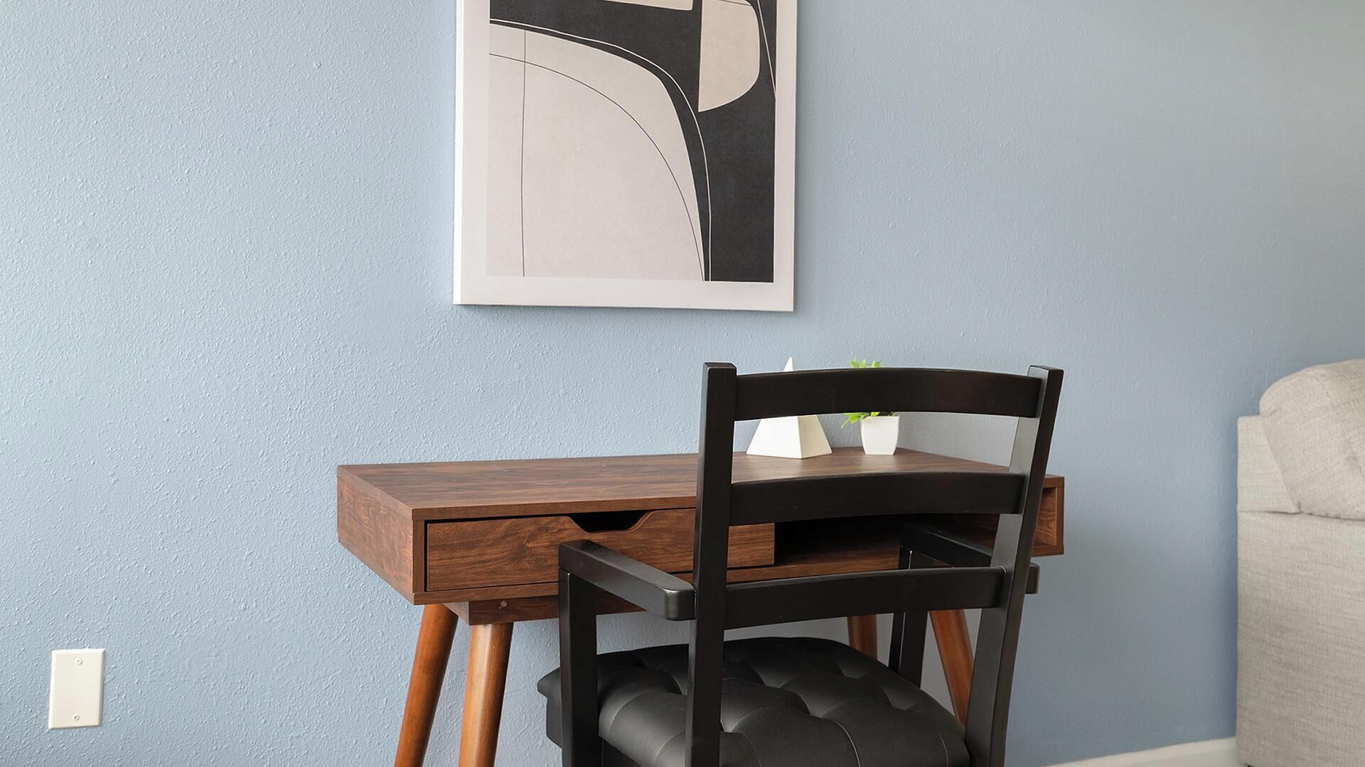 A desk with a chair, a wall-mounted artwork, and a light switch.