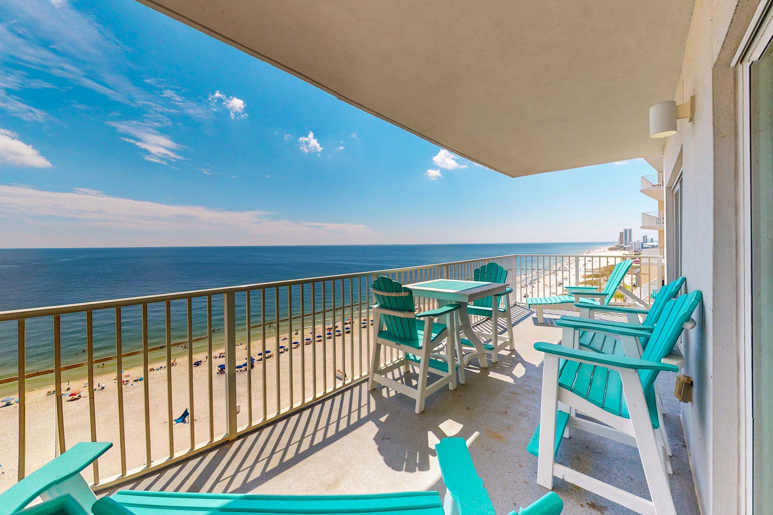 A balcony with a view of the beach and ocean, outdoor furniture, and a railing.