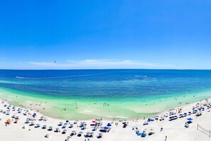 A beach with clear blue water, white sand, and umbrellas. - Waterfront condo w/ swim through indoor/outdoor community pools, hot tub & sauna (Gulf Shores)