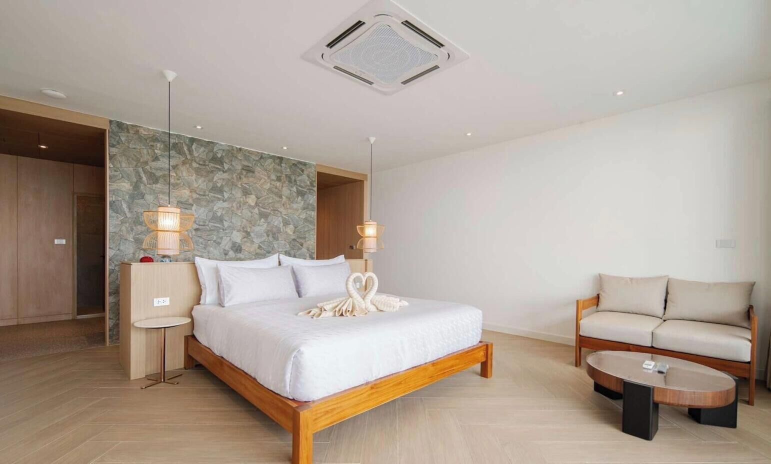 A modern hotel room with a large bed, a sofa, a round coffee table, and a stone accent wall.