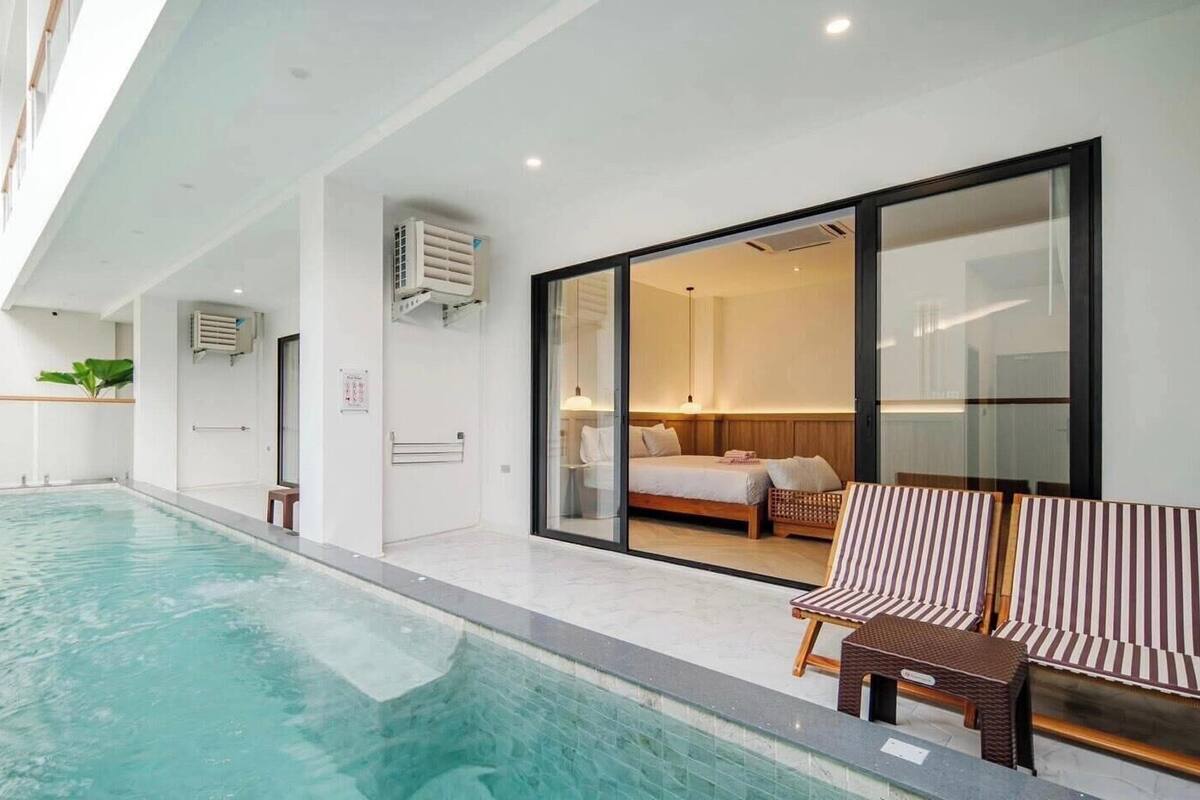 A modern hotel room with a large window, a bed, a small seating area, and a pool.