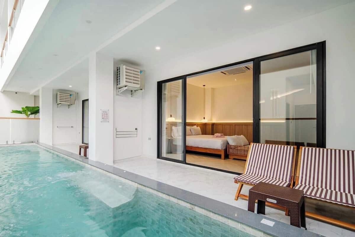 Una habitación de hotel moderna con un ventanal grande, una cama, una mesita y una zona de piscina.