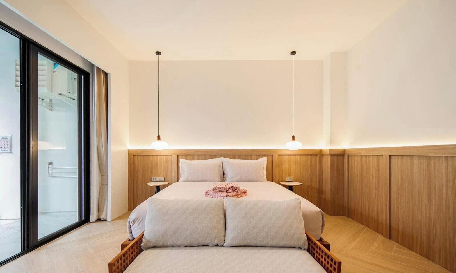 A modern bedroom with a large bed, wooden headboard, bedside tables, and a sliding glass door leading to a bathroom.