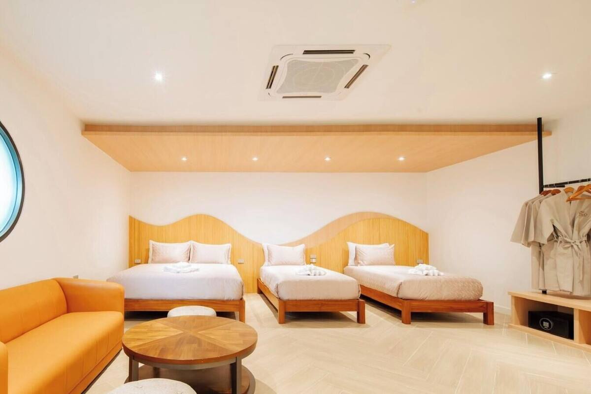 A hotel room with two beds, a round wooden table, an orange sofa, and a round mirror.