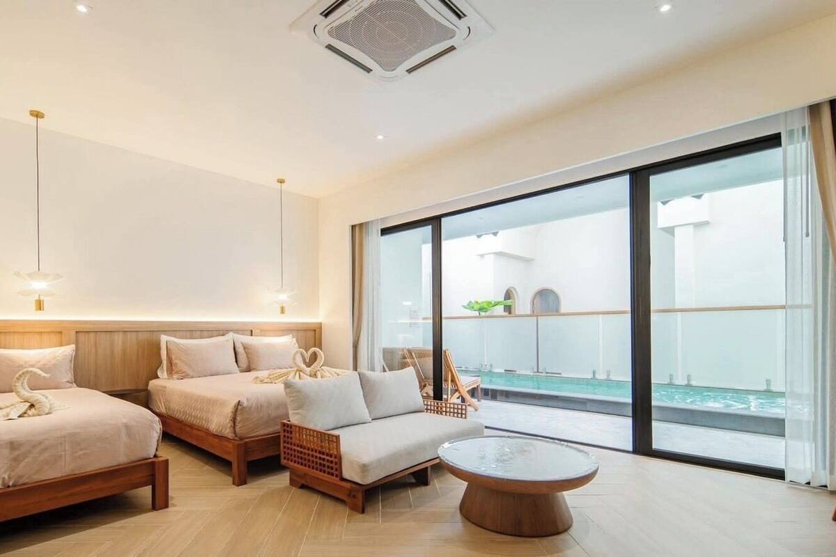 A modern hotel room with a large balcony, two beds, a sofa, and a round coffee table.