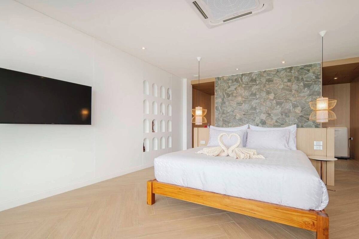 A modern hotel room with a large bed, a flat-screen TV, a stone accent wall, and a wooden floor.