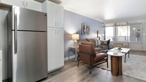 Een moderne keuken met een roestvrijstalen koelkast, witte kasten, een eethoek met tafel en stoelen, en een raam met uitzicht.