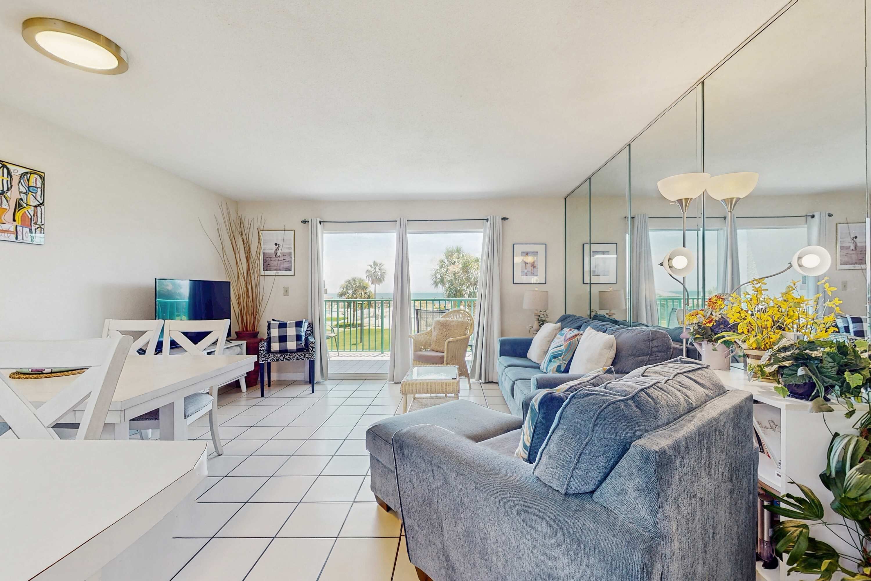 Ein modernes Wohnzimmer mit grauem Sofa, einem Esstisch und einem Balkon mit Blick auf Grünflächen.