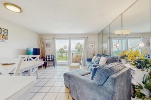 Ein modernes Wohnzimmer mit grauem Sofa, einem Esstisch und einem Balkon mit Blick auf Grünflächen.