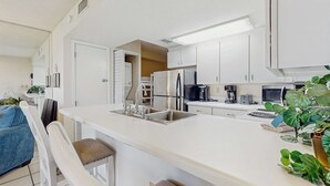 A modern kitchen with white cabinets, a stainless steel refrigerator, a coffee maker, and a sink. - Waterfront condo with shared pool & hot tub - near beach at Plantation Palms (Fort Morgan)