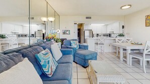 A modern living room with a sofa set, a dining table with chairs, and a kitchen area visible through an open door. - Waterfront condo with shared pool & hot tub - near beach at Plantation Palms (Fort Morgan)