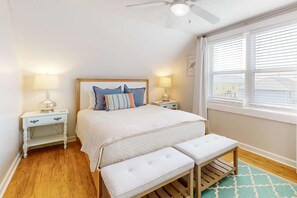 A bedroom with a bed, two bedside tables, a bench, a ceiling fan, and a window with blinds. - Dreamy, dog-friendly, coastal retreat with screened porch - walk to the beach (Fort Morgan)