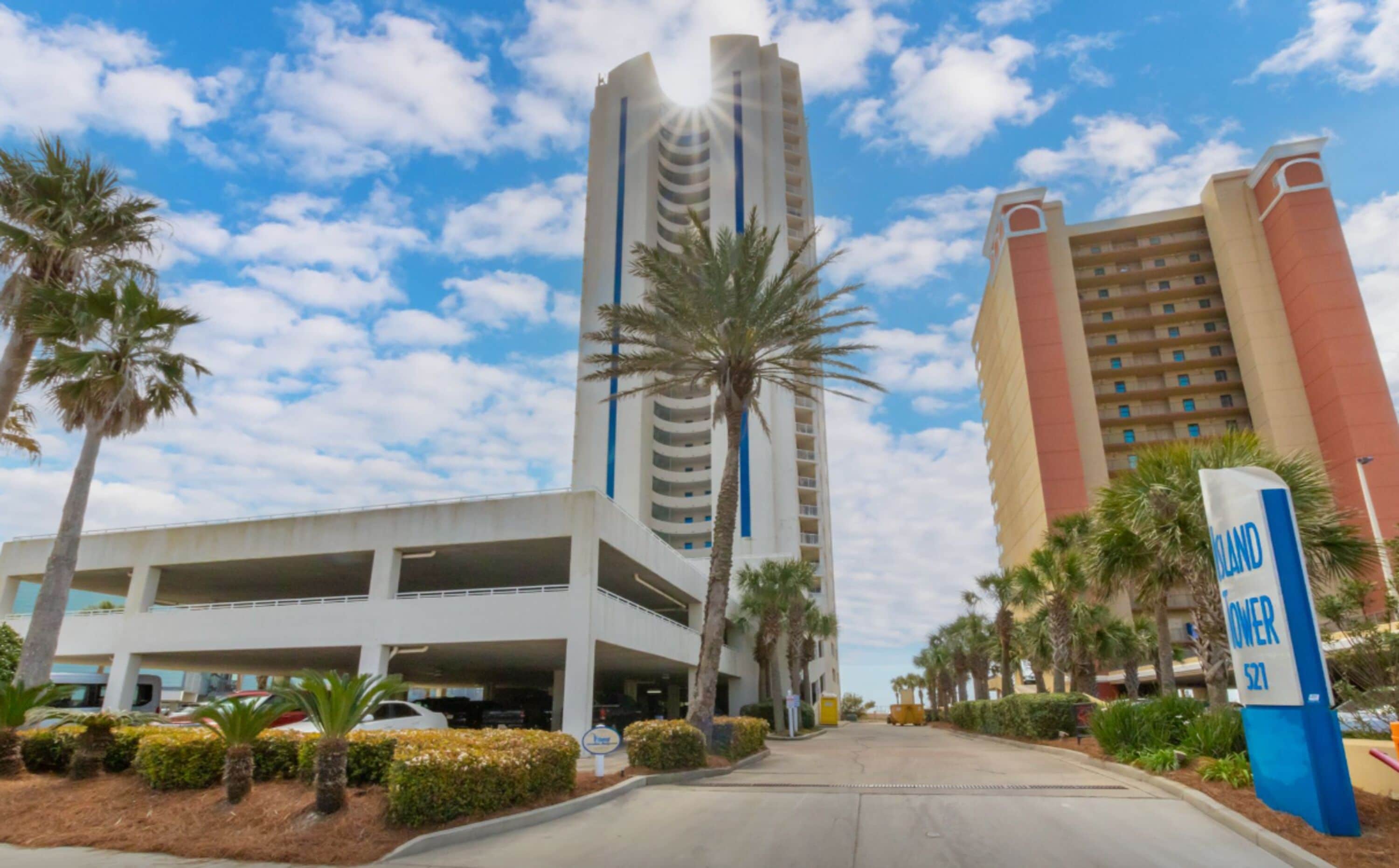 A hotel with a parking garage, palm trees, and a clear sky.