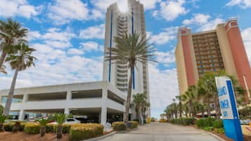 A hotel with a parking garage, palm trees, and a clear sky.