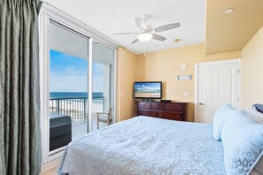 Een slaapkamer met een bed, een televisie, een dressoir, een deur en uitzicht op zee.