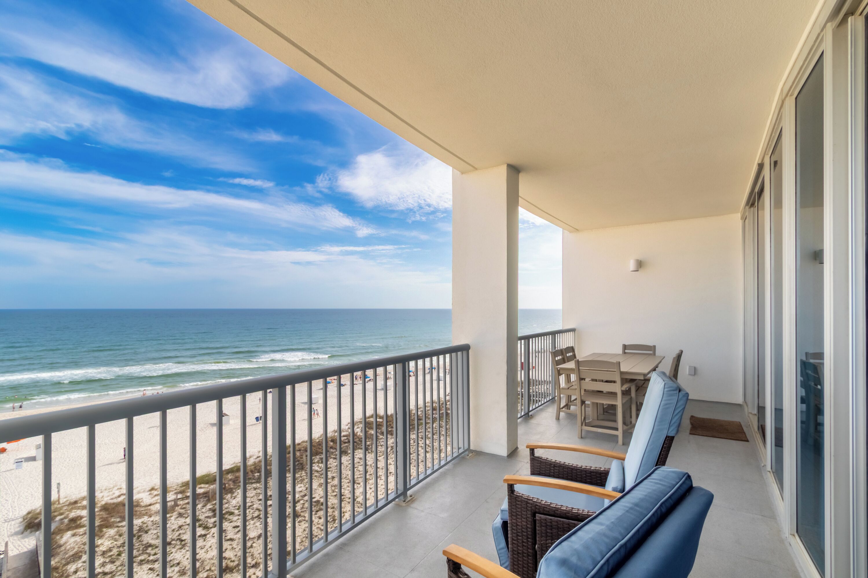 Un balcon avec vue sur la plage et l’océan, une table avec des chaises et une porte vitrée.