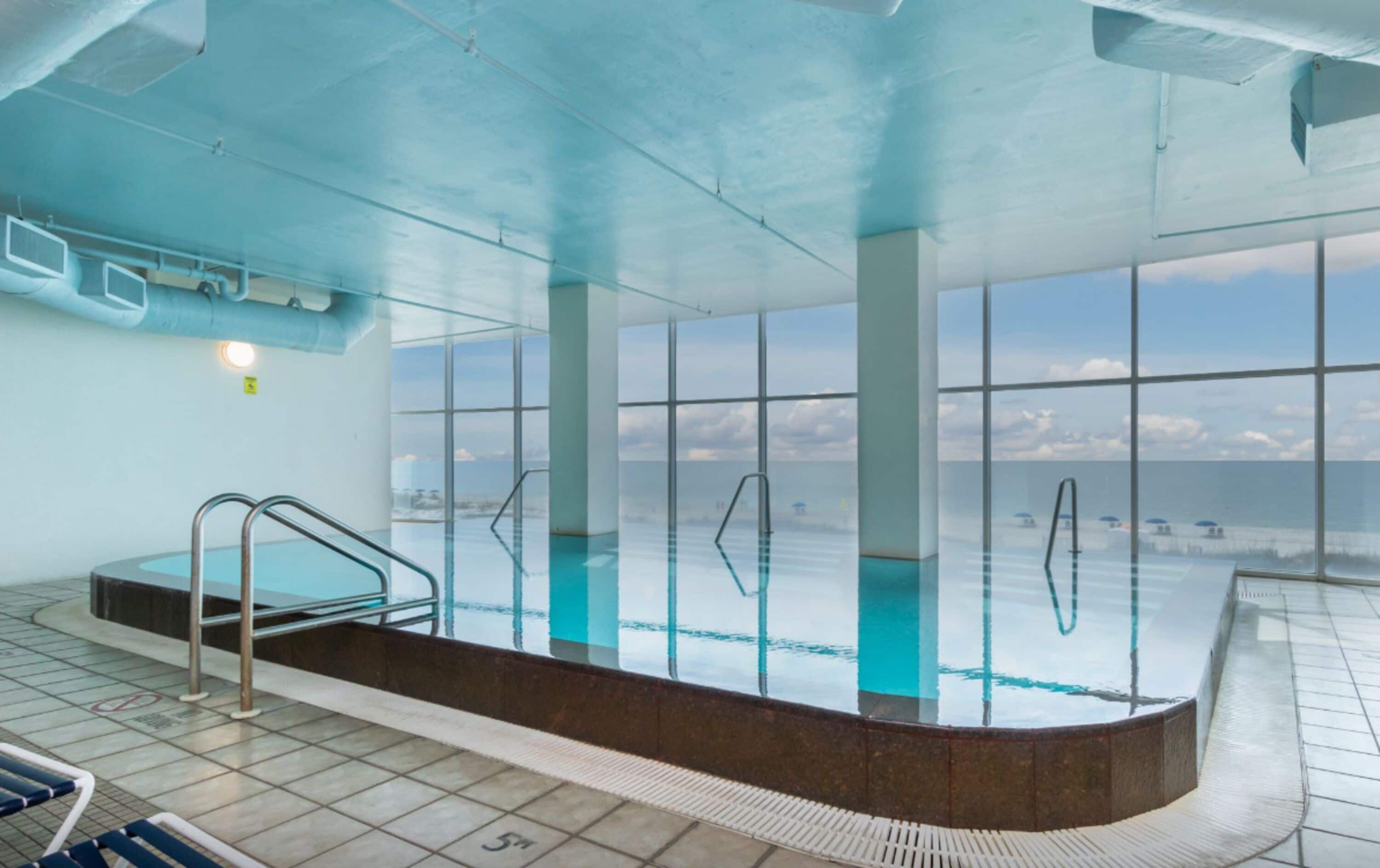 Una piscina interna con pareti in vetro trasparente, un trampolino e un pavimento piastrellato.
