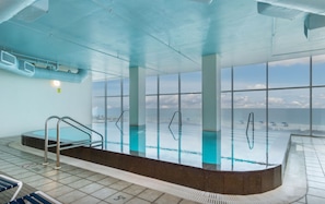 An indoor swimming pool with clear glass walls, a diving board, and a tiled floor. - Island Tower 701 (Gulf Shores)